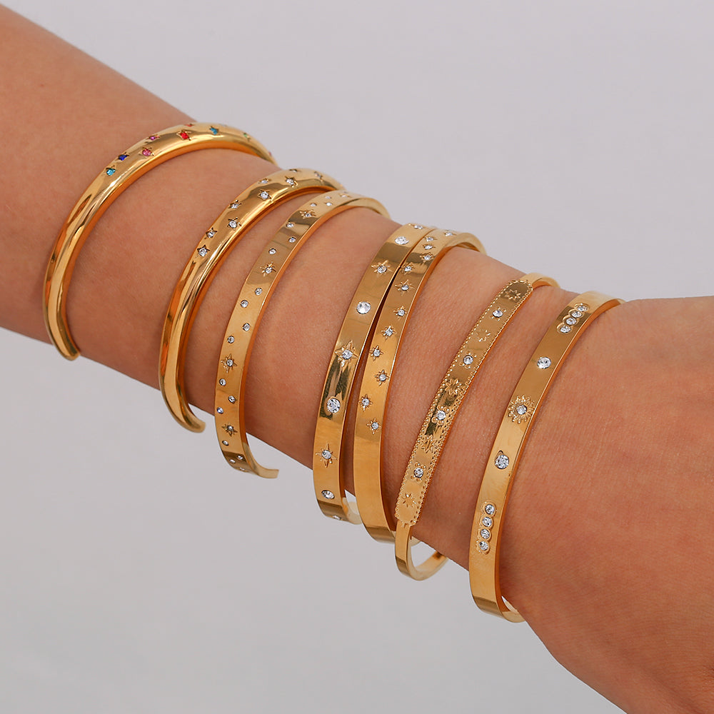 Pulsera o brazalete rígido tipo esclava resistente al agua. Está confeccionado en acero inoxidable con baño de oro 18 kilates o plata rodiada. tiene circonitas en forma de estrellas.Gold plated stainless Steel stiff or rigid waterproof rainbow zircon star bangle bracelet.
