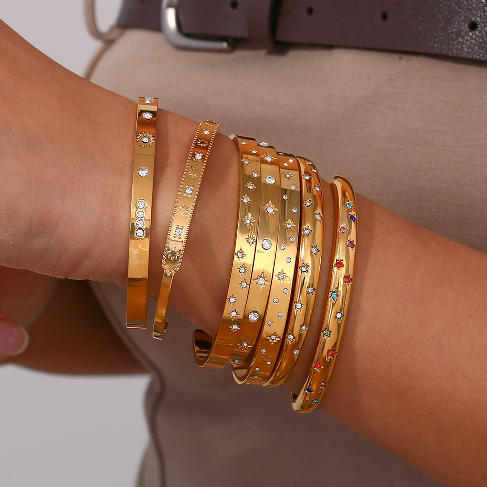 Pulsera o brazalete rígido tipo esclava resistente al agua. Está confeccionado en acero inoxidable con baño de oro 18 kilates o plata rodiada. tiene circonitas en forma de estrellas.Gold plated stainless Steel stiff or rigid waterproof rainbow zircon star bangle bracelet.