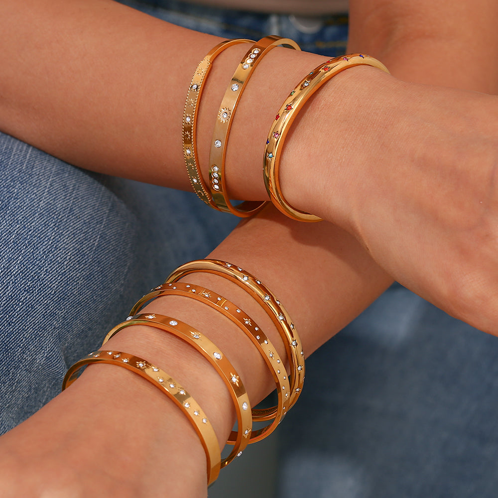 Pulsera o brazalete rígido tipo esclava resistente al agua. Está confeccionado en acero inoxidable con baño de oro 18 kilates o plata rodiada. tiene circonitas en forma de estrellas.Gold plated stainless Steel stiff or rigid waterproof rainbow zircon star bangle bracelet.