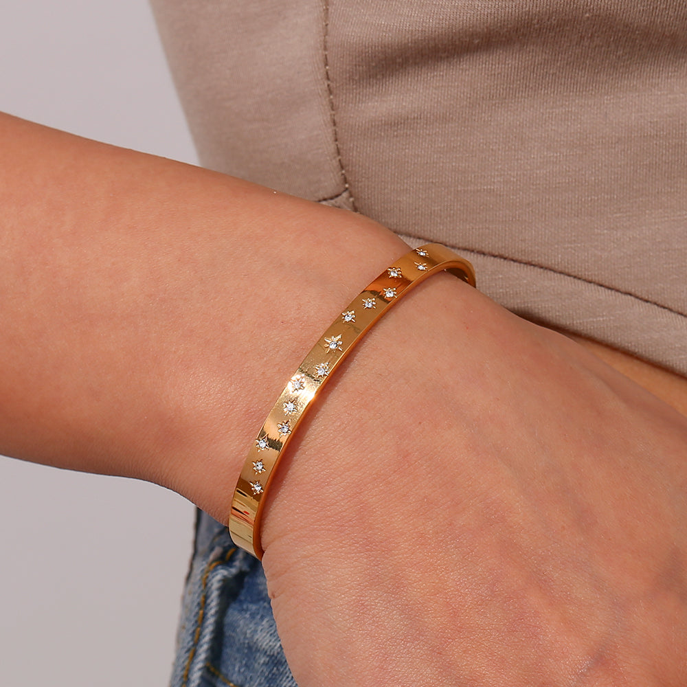 Pulsera o brazalete rígido tipo esclava resistente al agua. Está confeccionado en acero inoxidable con baño de oro 18 kilates o plata rodiada. tiene circonitas en forma de estrellas.Gold plated stainless Steel stiff or rigid waterproof rainbow zircon star bangle bracelet.