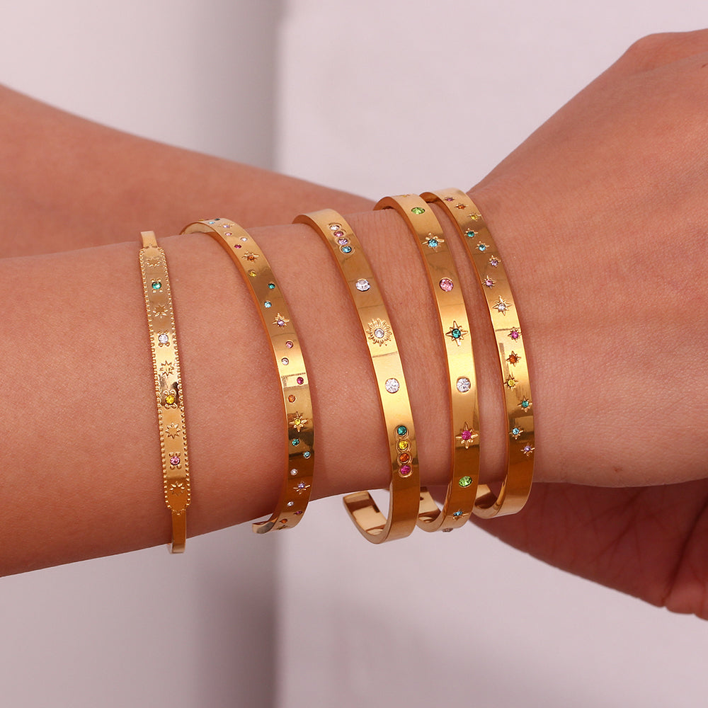 Pulsera o brazalete rígido tipo esclava resistente al agua. Está confeccionado en acero inoxidable con baño de oro 18 kilates o plata rodiada. tiene circonitas en forma de estrellas.Gold plated stainless Steel stiff or rigid waterproof rainbow zircon star bangle bracelet.
