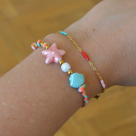 pulsera DE VERANO waterproof o resistente al agua confeccionada con cordón rosa con abalorios de cerámica y acero dorado. Cierre ajustable, colgante de estrella de mar y concha en color rosa y azul turquesa. Ideal para regalar a mujeres, niñas y adolescentes en vacaciones.