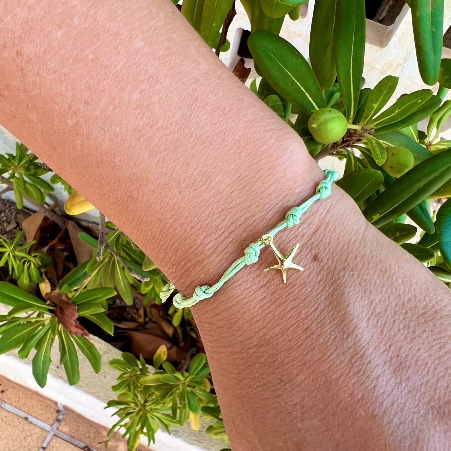 Pulsera para verano con nudos de colores. Está confeccionada en cordón encerado con dos nudos. Se puede personalizar con un colgante de letra o charms de estrella, concha o luna. El cierre es ajustable.