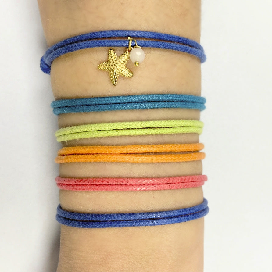 Pulsera para verano de colores. Está confeccionada en cordón encerado con dos nudos. Se puede personalizar con un colgante de letra o charms de estrella, concha o luna. El cierre es ajustable.