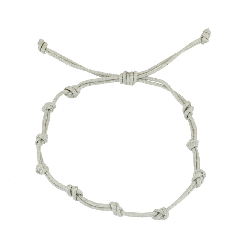 Pulsera para verano con nudos de color gris claro. Está confeccionada en cordón encerado con dos nudos. Se puede personalizar con un colgante de letra o charms de estrella, concha o luna. El cierre es ajustable.