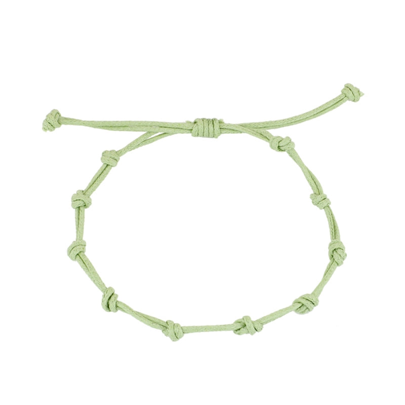 Pulsera para verano con nudos de colore verde palo. Está confeccionada en cordón encerado con dos nudos. Se puede personalizar con un colgante de letra o charms de estrella, concha o luna. El cierre es ajustable.