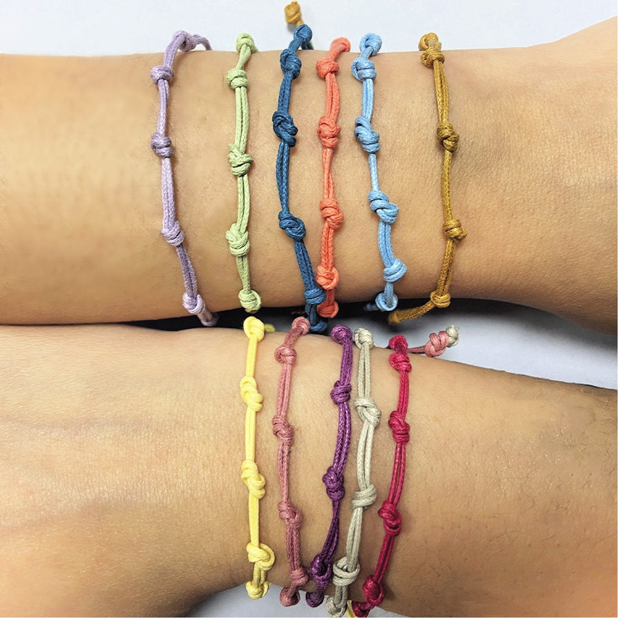 Pulsera para verano con nudos de colores. Está confeccionada en cordón encerado con dos nudos. Se puede personalizar con un colgante de letra o charms de estrella, concha o luna. El cierre es ajustable.