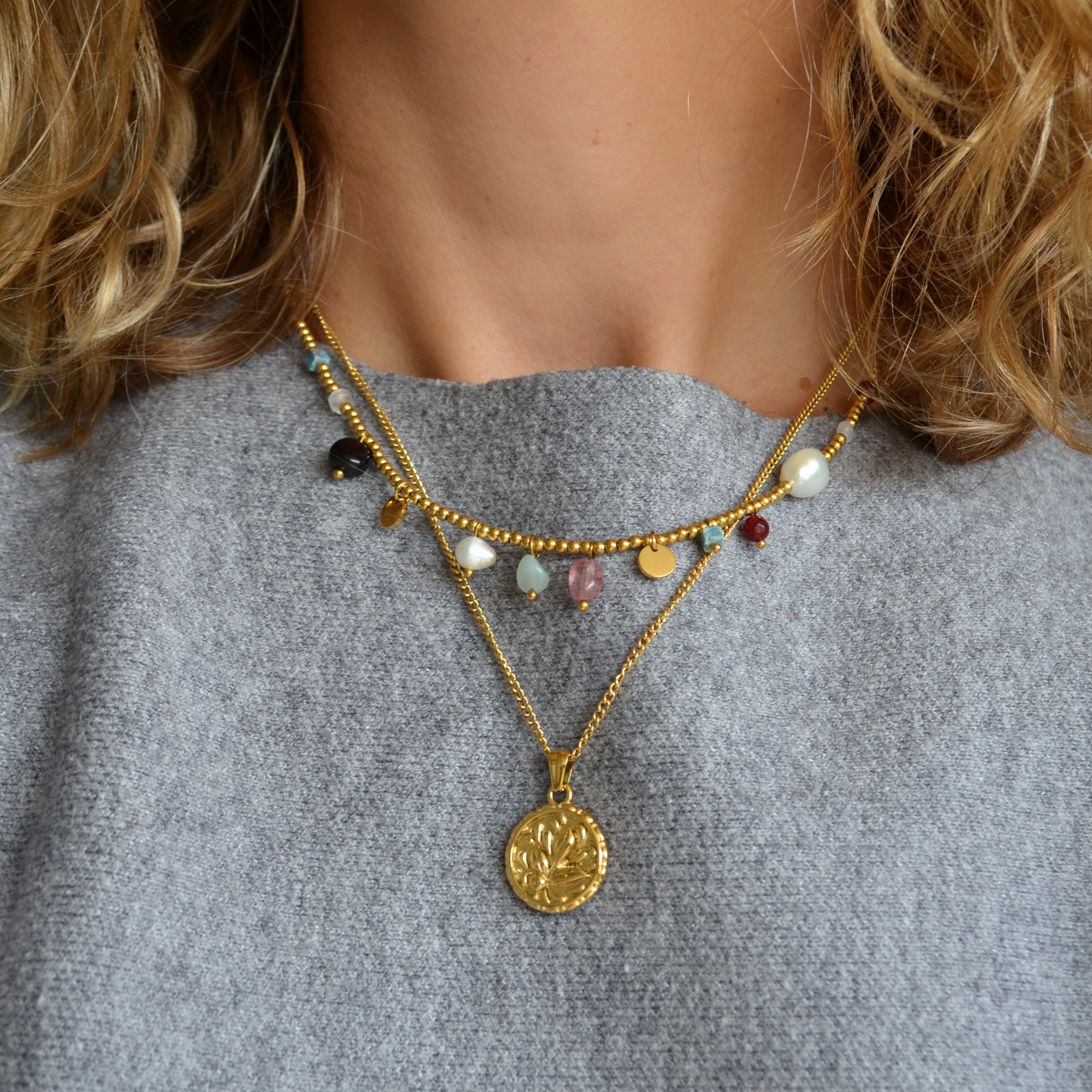 COLLAR waterproof o resistente al agua confeccionada en acero con baño de oro 18 kilates. Tiene abalorios de colores imitando piedra natural y perla cultivada. 