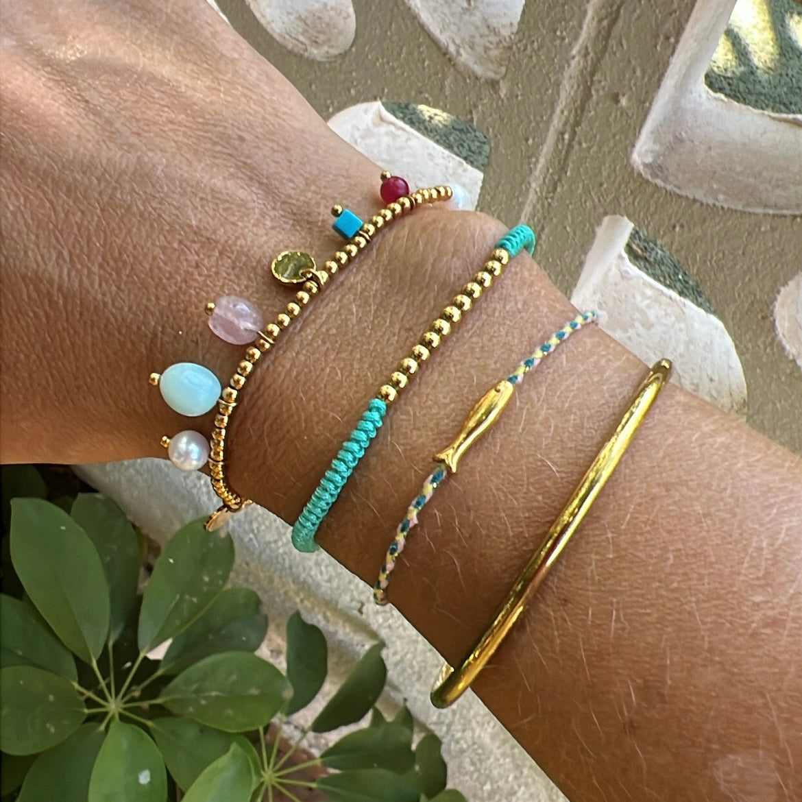 pulsera elástica waterproof o resistente al agua confeccionada en acero con baño de oro 18 kilates. Tiene abalorios de colores imitando piedra natural y perla cultivada. 
