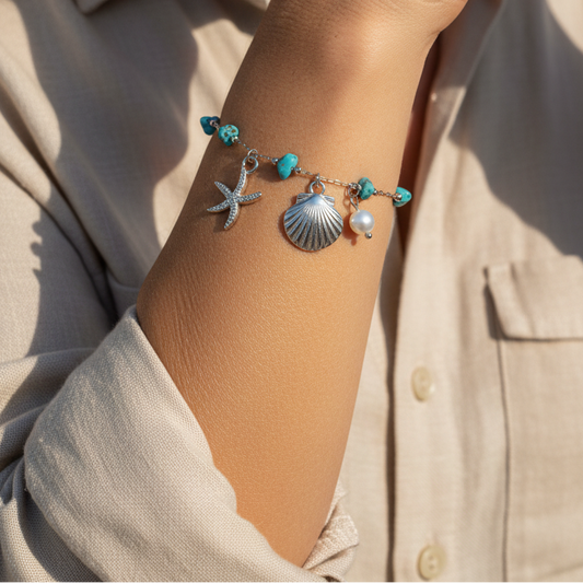 pulsera waterproof o resistente al agua confeccionada en acero con baño de oro 18 kilates. Tiene abalorios de colores imitando piedra natural turqyesa y perla cultivada. también tiene colgantes de estrella de mar y concha. 
