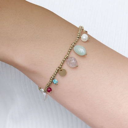 pulsera elástica waterproof o resistente al agua confeccionada en acero con baño de oro 18 kilates. Tiene abalorios de colores imitando piedra natural y perla cultivada. 