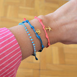 Pulsera para verano con nudos de colores. Está confeccionada en cordón encerado con dos nudos. Se puede personalizar con un colgante de letra o charms de estrella, concha o luna. El cierre es ajustable.
